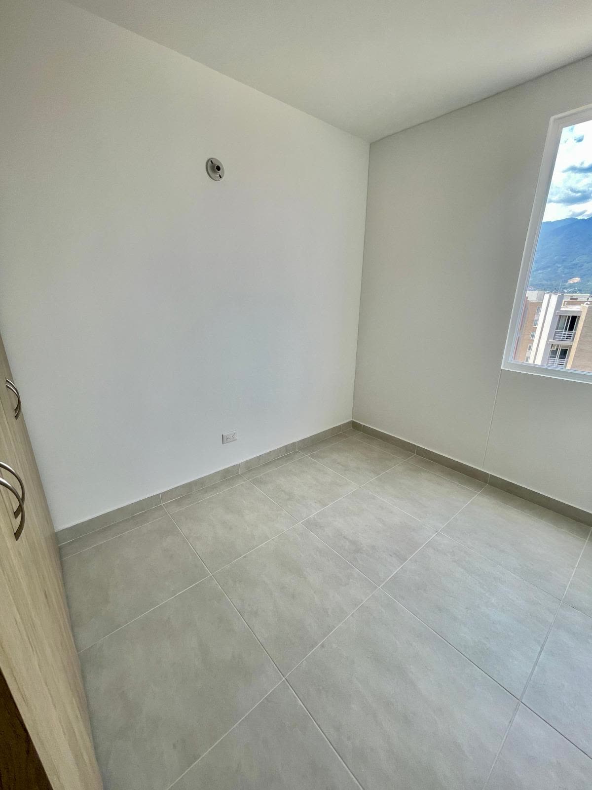 Habitación vacía con ventana y vista a las montañas y a otros edificios